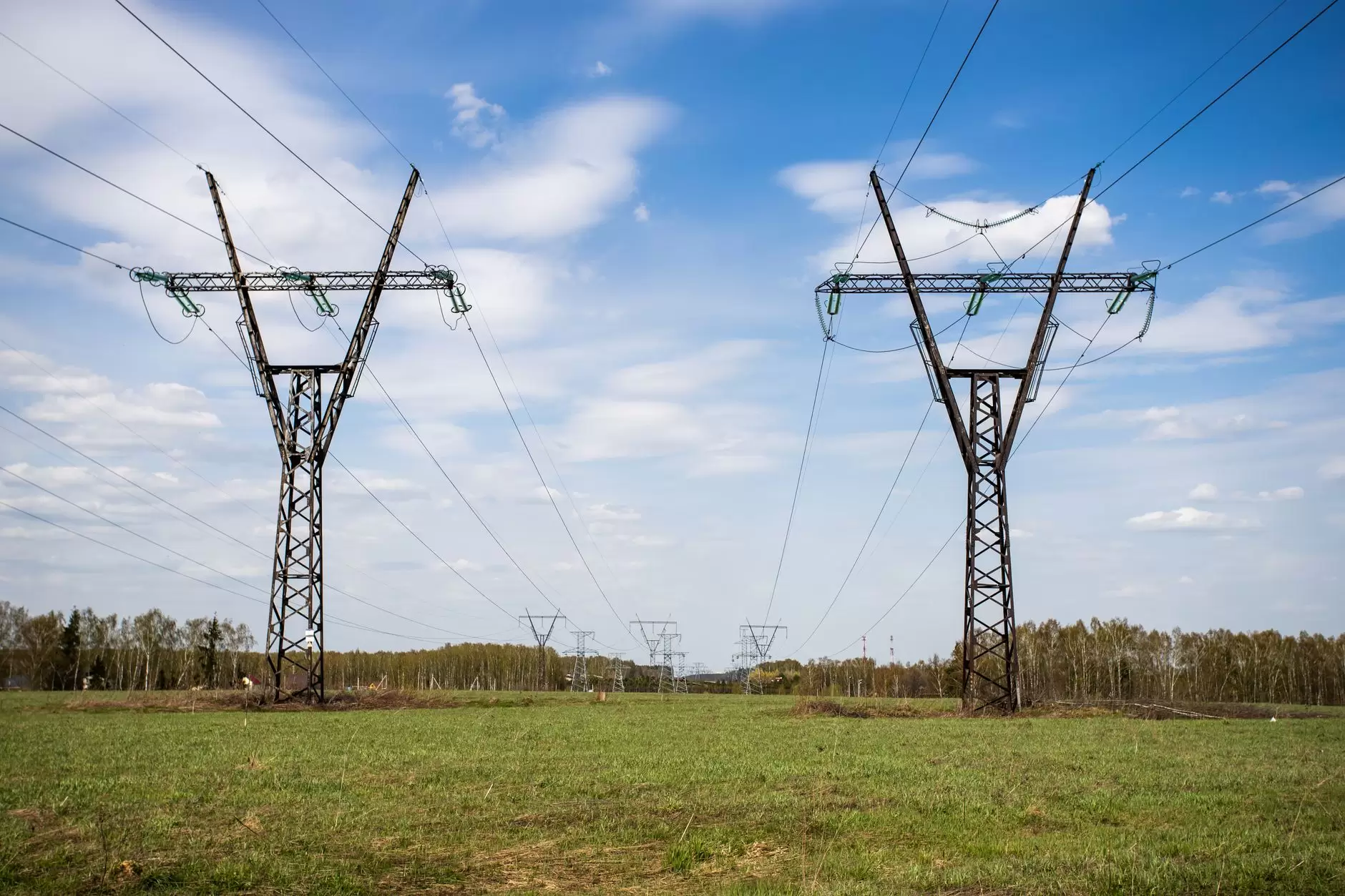Transmission Infrastructure: How the High-Voltage Grid Moves Power — high-voltage transmission towers crossing a rural landscape under a partly cloudy sky
