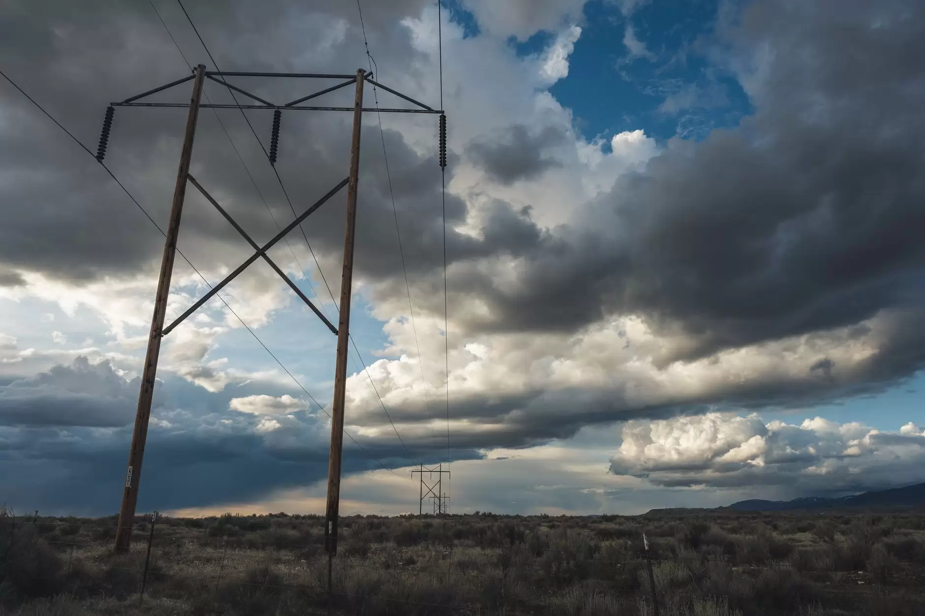 HVDC Explained: LCC vs. VSC Converters and Where Each Wins — high-voltage transmission towers crossing a broad rural landscape under dramatic clouds