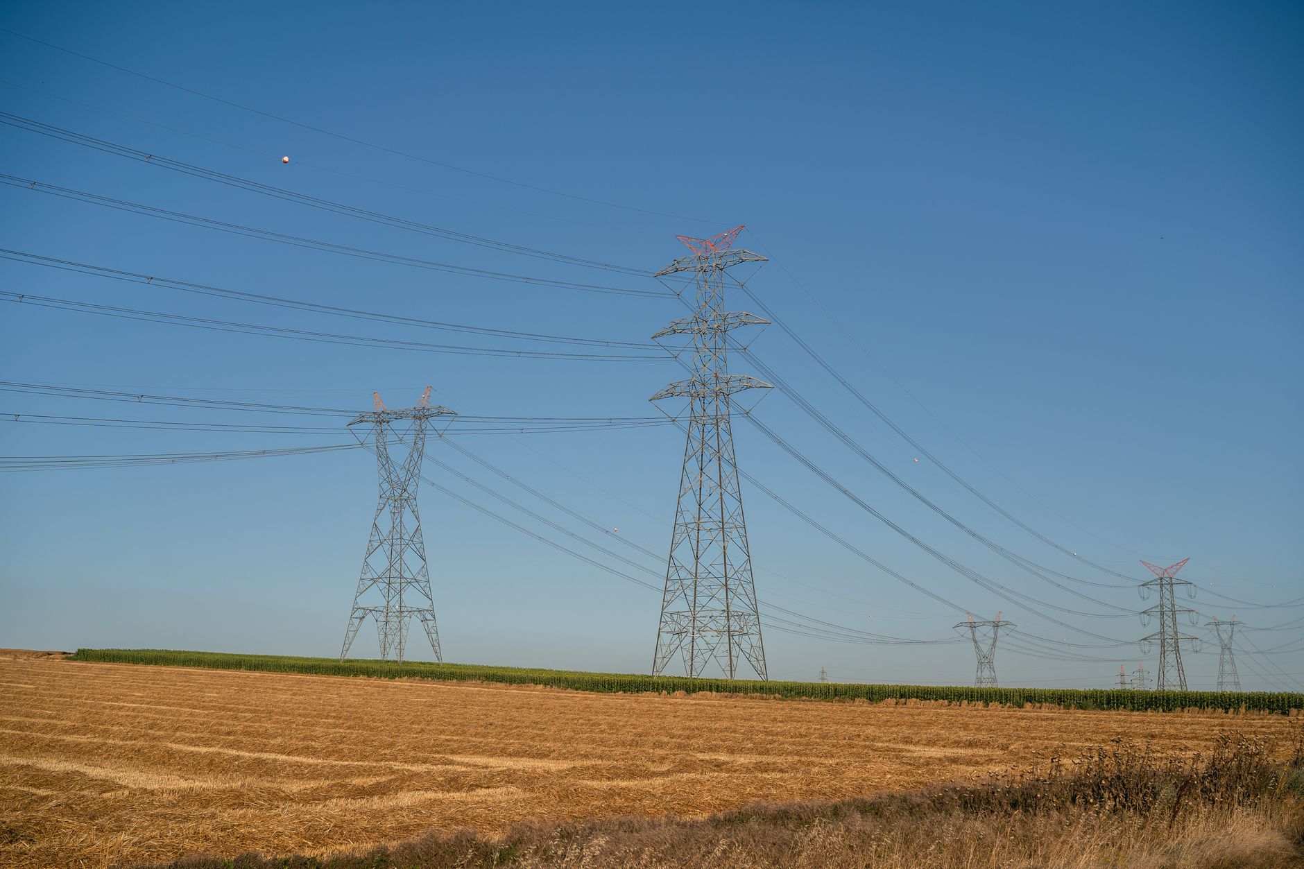 Transmission Permitting: The Institutional Maze Across Multiple Jurisdictions — high-voltage transmission towers crossing rural farmland near a state border