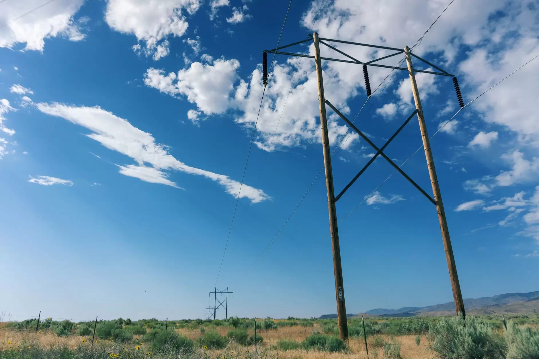 Grid-Enhancing Technologies: How Dynamic Line Rating and Other Tools Unlock Capacity from Existing Lines — high-voltage transmission towers crossing a windy open landscape under moving clouds