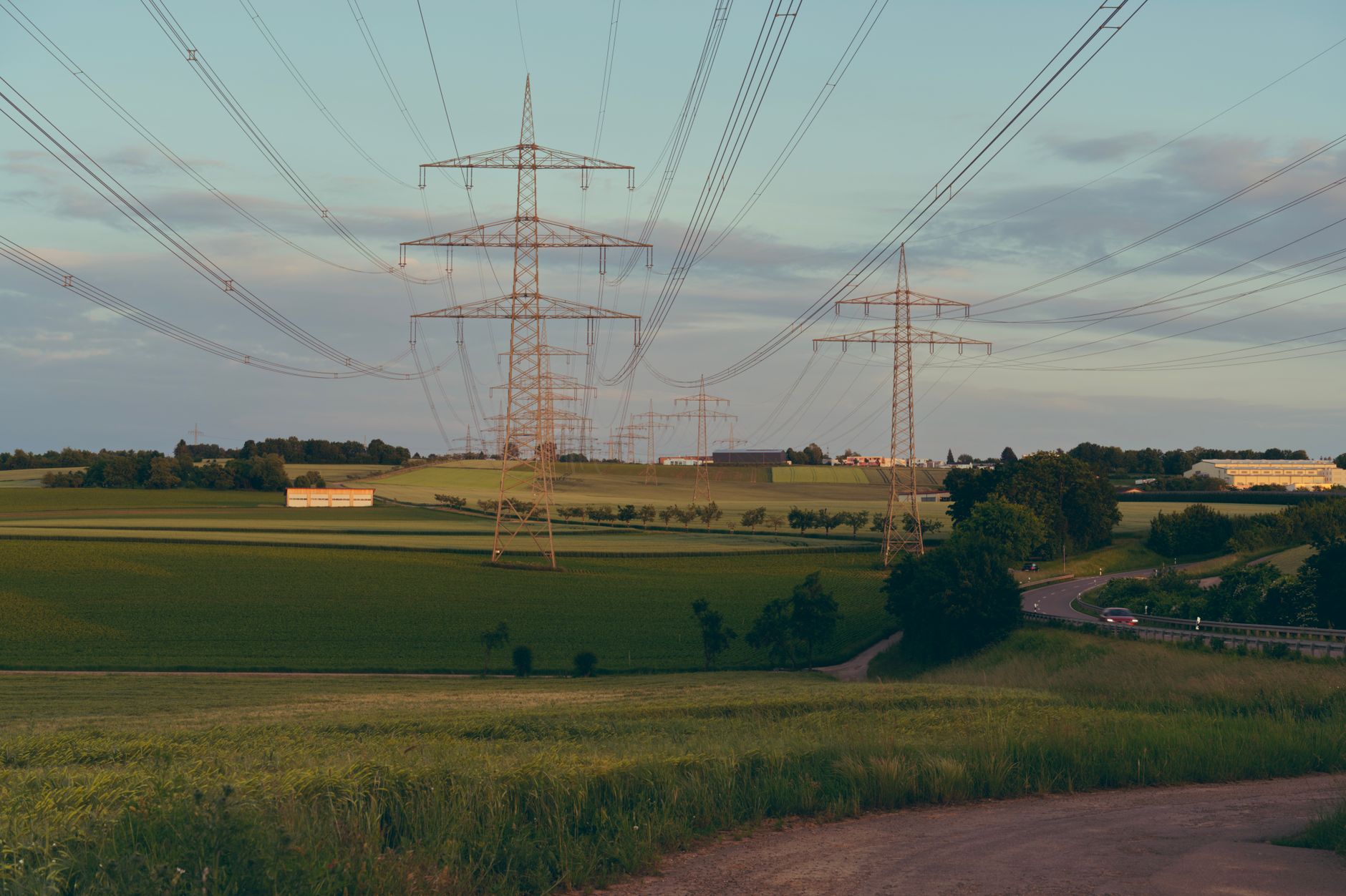 Transmission Permitting: The Institutional Maze Across Multiple Jurisdictions — high-voltage transmission towers crossing rural farmland with roads and scattered homes