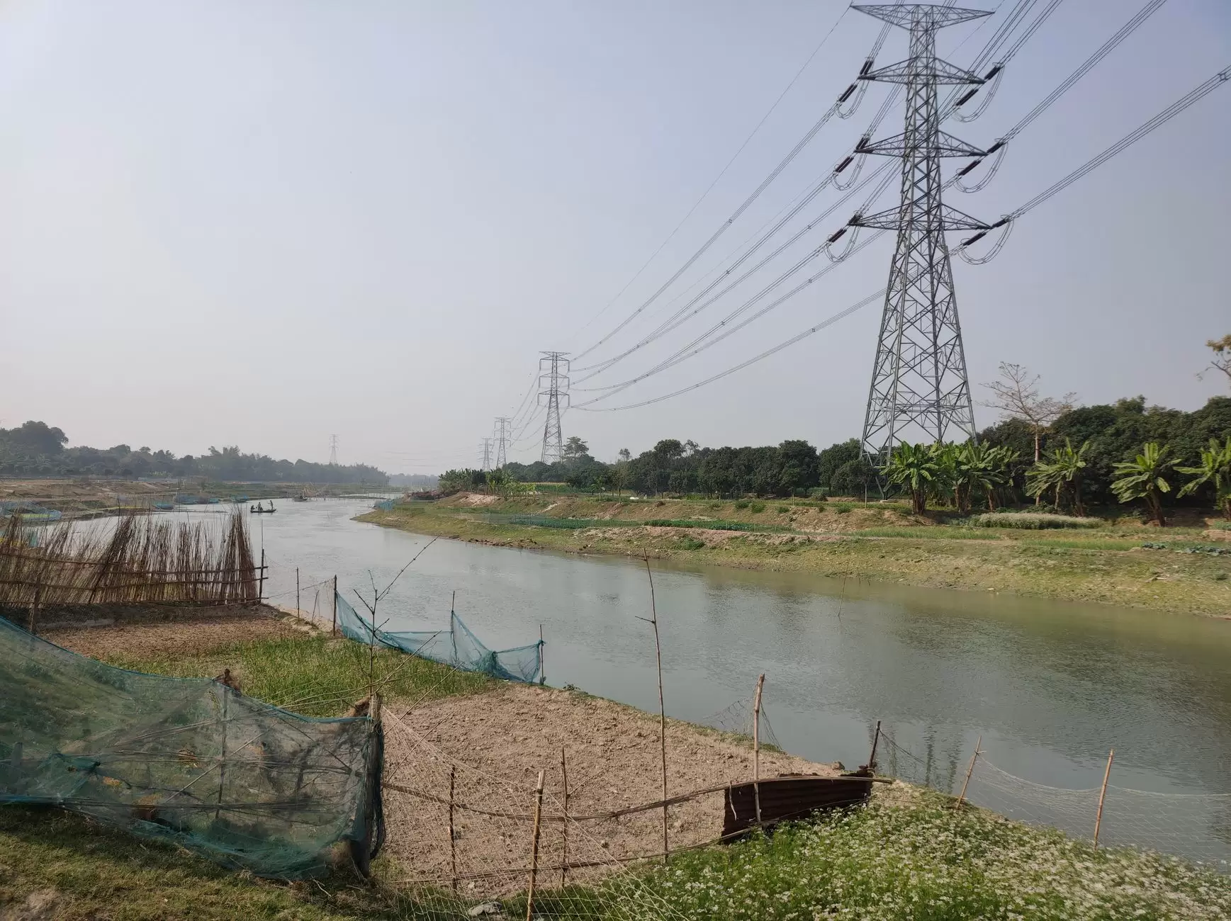 Harmonizing Grid Codes: The Technical Key to Regional Power Integration — high-voltage power interconnector towers crossing a river between rural landscapes