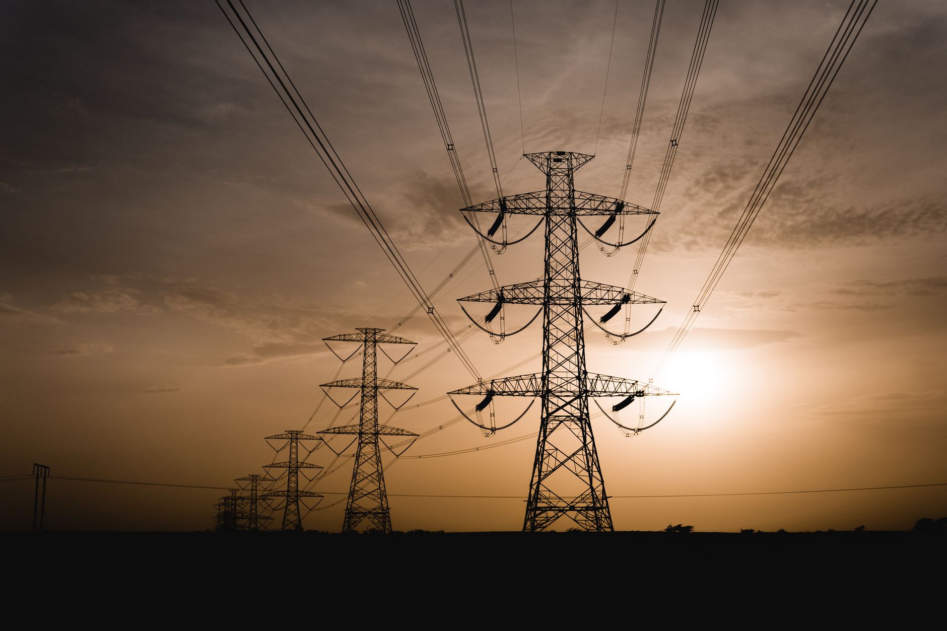 How Grid-Scale Batteries Make Money: The Markets from Regulation to Black Start — utility-scale battery storage containers beside high-voltage transmission lines at sunset