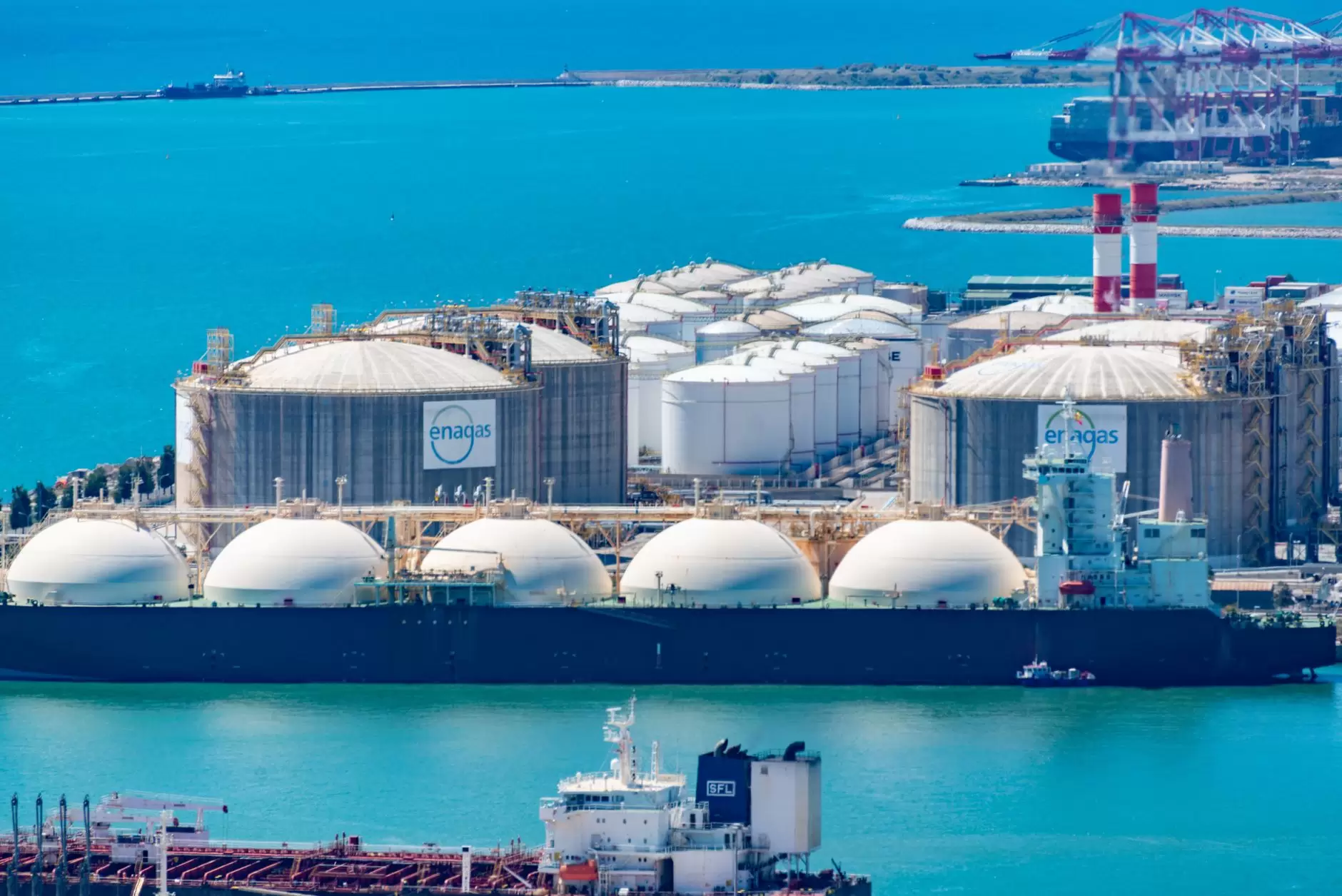 Japan's GX Strategy: Where Decarbonization Meets Energy Security — Japanese coastal power plant with fuel storage tanks and cargo ships under cloudy skies