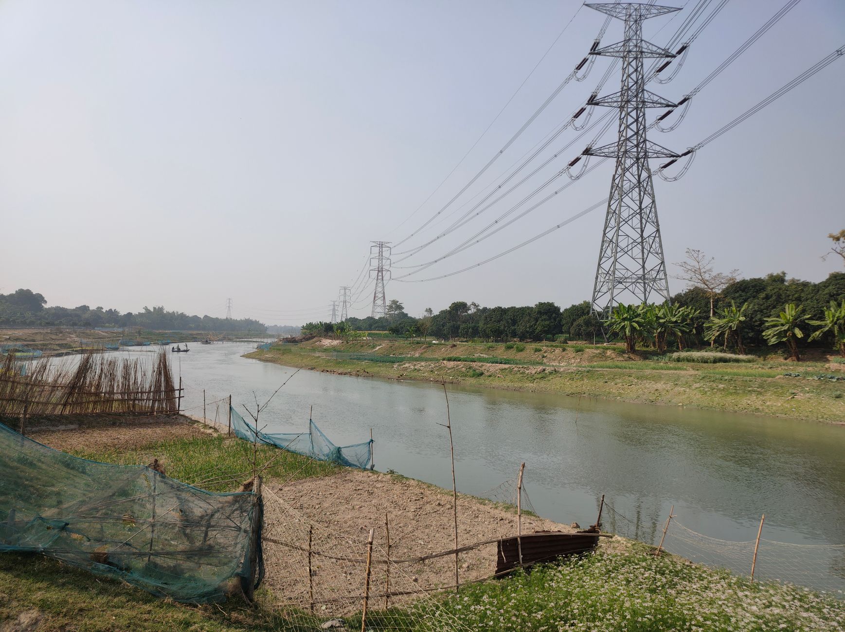 Overcoming the Barriers to Cross-Border Power Trading: Tariffs, Regulation, and Infrastructure — high-voltage transmission towers crossing a river between rural landscapes