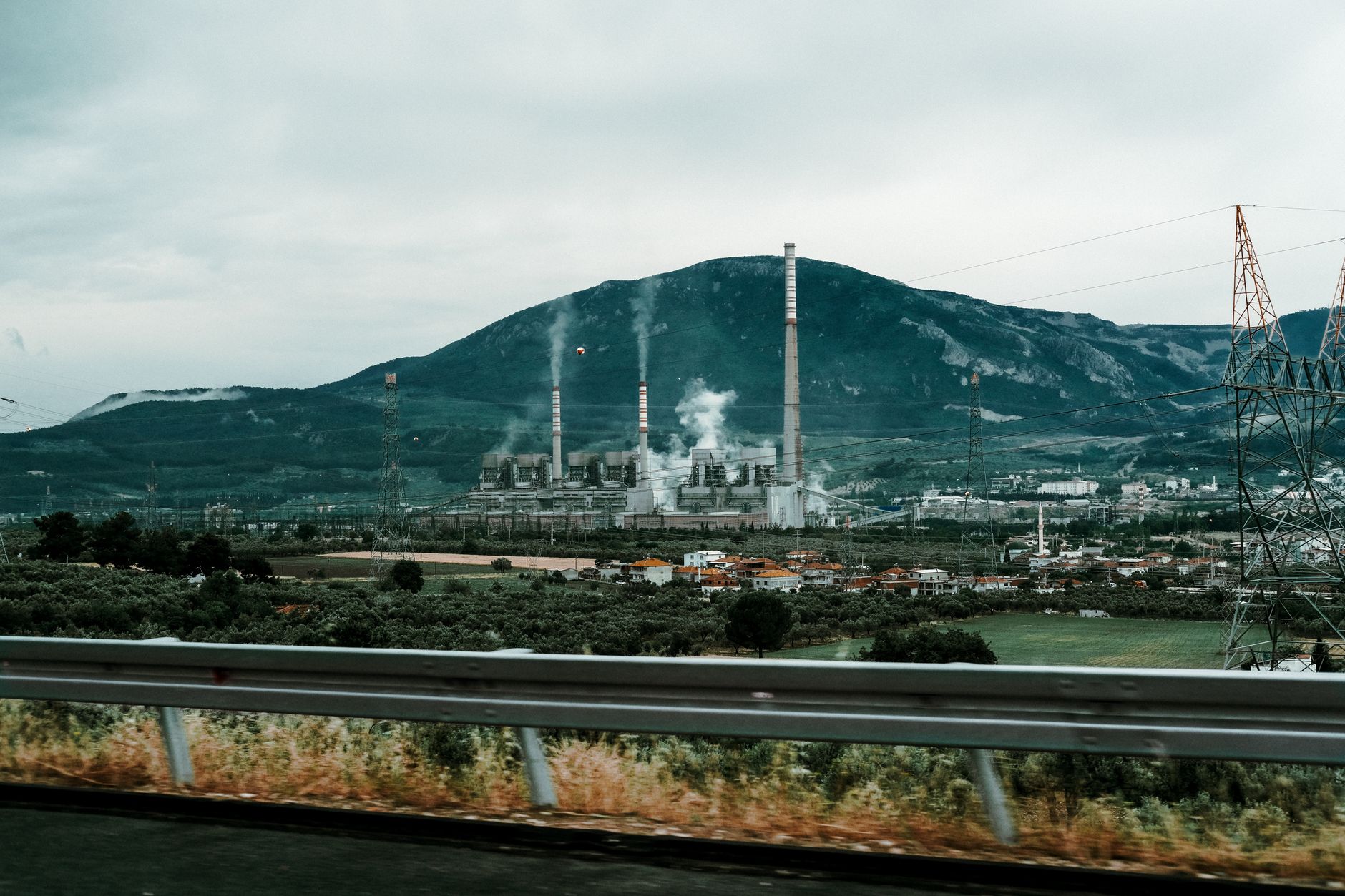 A Simple Guide to Carbon Markets: Cap-and-Trade, Offsets, and Carbon Taxes — industrial facility smokestacks beside electricity transmission towers under overcast sky