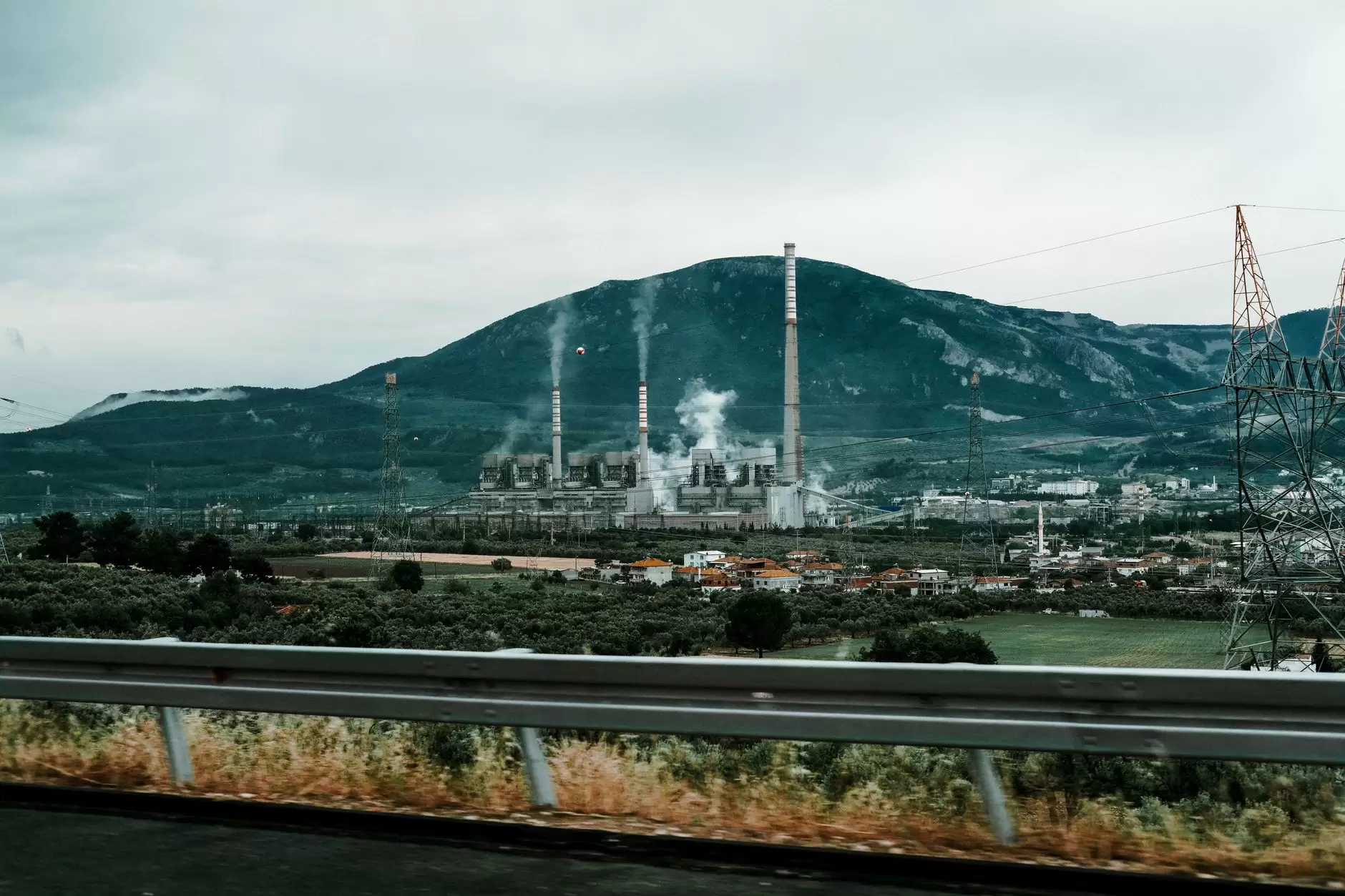 A Simple Guide to Carbon Markets: Cap-and-Trade, Offsets, and Carbon Taxes — industrial facility smokestacks beside electricity transmission towers under overcast sky