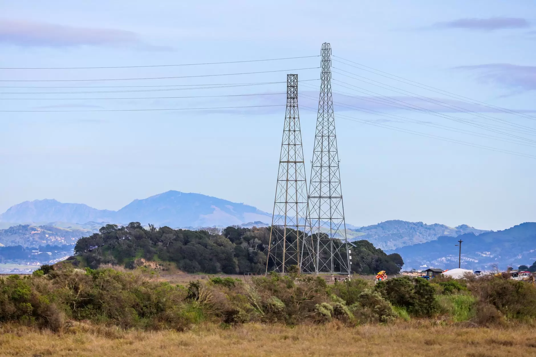 India to Singapore: What a 2 GW Power Corridor Requires — high-voltage transmission towers crossing tropical hills and rural landscape